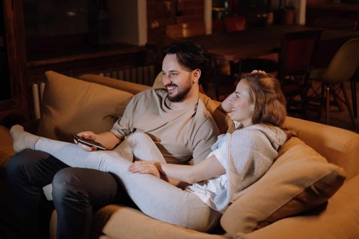 Married couple sitting on couch comfortably laughing and discussing prenups after marriage during ad break.
