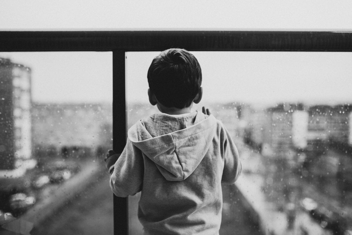 Grayscale photo of young child looking out window pondering parental alienation laws in Australia