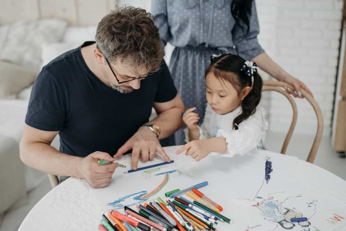 Paternal figure knows how to become a legal guardian of a child in Australia and is with a young girl drawing with colouring pencils